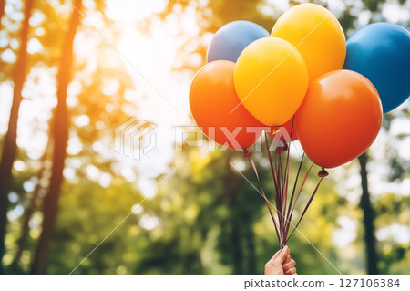 Vintage Style Photo of Hand Holding Colorful Balloons in a Sunlit Forest Setting 127106384