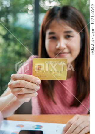 Woman displaying a gold credit card, emphasizing finance and banking themes, with a natural green backdrop. Woman displaying a gold credit card, emphasizing finance and banking themes, with a natural green backdrop. 127106549