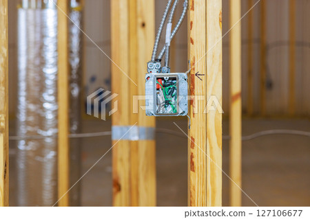 Construction workers install an electrical box in newly framed room while building house. 127106677