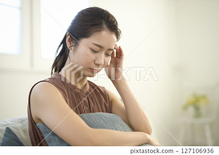 A woman in her 20s who is feeling unwell sitting on a sofa A woman in her 20s who is feeling unwell sitting on a sofa 127106936