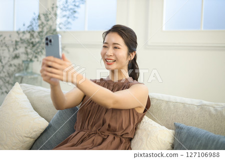 A woman in her twenties sitting on a sofa and operating a smartphone 127106988