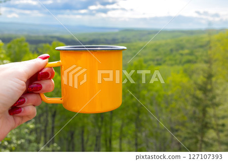 Hiker's female hand is holding a yellow camping cup. 127107393