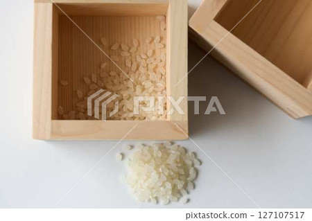 A small amount of rice in a wooden box and spilled rice on a white background 127107517