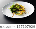 Grilled bok choy garnished with fresh herbs and drizzled with sauce on a sleek black background. 127107929