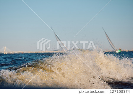 Sailing regatta in the Gulf of Finland at sunset, two sailing yachts competing in a race, splashing water from under the boats, teamwork, board the boat 127108574