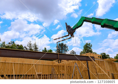 Heavy telehandler machinery lifts steel beam at construction site surrounded by wooden frames Heavy telehandler machinery lifts steel beam at construction site surrounded by wooden frames 127108605