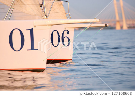 Sailing regatta in the Gulf of Finland at sunset, two sailing yachts competing in a race, splashing water from under the boats, teamwork, board the boat 127108608