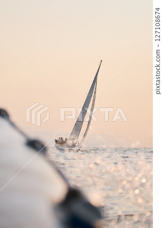 Sailing regatta in the Gulf of Finland at sunset, sailing yacht competing in a race, splashing water from under the boat, teamwork, board the boat Sailing regatta in the Gulf of Finland at sunset, sailing yacht competing in a race, splashing water from under the boat, teamwork, board the boat 127108674