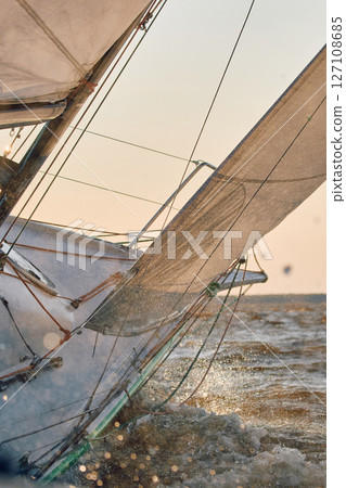 Sailing regatta in the Gulf of Finland at sunset, sailing yacht competing in a race, splashing water from under the boat, teamwork, board the boat Sailing regatta in the Gulf of Finland at sunset, sailing yacht competing in a race, splashing water from under the boat, teamwork, board the boat 127108685