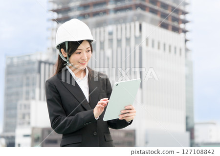 一位身穿西裝、頭戴頭盔的年輕女子操作平板電腦；施工經理、現場主管、女土木工程師 127108842