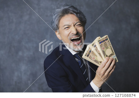 Smiling senior businessman holding a stack of bills Smiling senior businessman holding a stack of bills 127108874