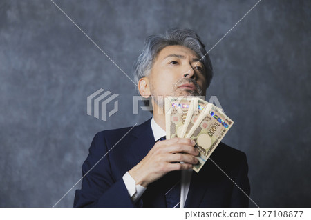 Smiling senior businessman holding a stack of bills 127108877