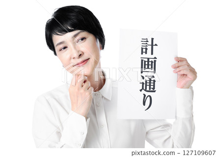 A middle-aged woman smiling and holding a piece of paper that says "As planned" A middle-aged woman smiling and holding a piece of paper that says "As planned" 127109607