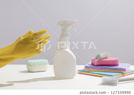 Yellow gloves and a white spray bottle rest on a clean table, surrounded by colorful cleaning cloths and brushes, prepared for household use. Mockup bottle unlabeled for design Yellow gloves and a white spray bottle rest on a clean table, surrounded by colorful cleaning cloths and brushes, prepared for household use. Mockup bottle unlabeled for design 127109998