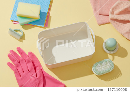An empty plastic tray is arranged with gloves, sponges, detergent brush and a sink on a yellow surface, showing the cleaning tools neatly arranged for daily tasks. An empty plastic tray is arranged with gloves, sponges, detergent brush and a sink on a yellow surface, showing the cleaning tools neatly arranged for daily tasks. 127110008