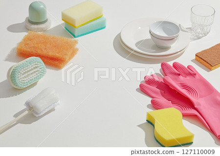 Colorful sponges, brushes, and gloves placed beside a few dishes, highlighting household cleaning essentials in a well-lit kitchen space. Copy space Colorful sponges, brushes, and gloves placed beside a few dishes, highlighting household cleaning essentials in a well-lit kitchen space. Copy space 127110009