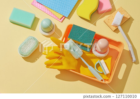 Multiple scrubbing pads, gloves, sponges and spray bottles scattered across a vibrant yellow surface, evoking energy and cleaning activity. Cleaner concept 127110010