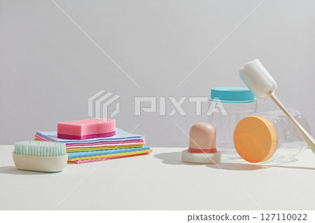A simple layout of kitchen cleaning items including scrub pads, brushes, and sponges, arranged neatly on a white surface. Concept of cleanliness, cleaning services. 127110022