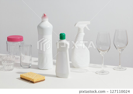 Group of cleaning bottles, brushes, and dish soap gathered with wine glasses, illustrating a kitchen cleanup scene. Mockup for cleansing products,cleaner concept 127110024