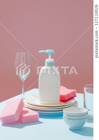 Single soap pump placed among dishes and wine glasses with shadows, standing out against a bright, pastel pink and blue-toned background. Ad template or package design for cleaning product Single soap pump placed among dishes and wine glasses with shadows, standing out against a bright, pastel pink and blue-toned background. Ad template or package design for cleaning product 127110026