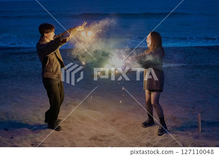 Young men and women playing hand-held fireworks on the beach at night Young men and women playing hand-held fireworks on the beach at night 127110048