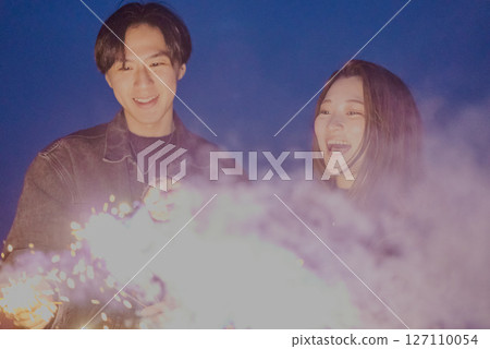 Young men and women playing hand-held fireworks on the beach at night Young men and women playing hand-held fireworks on the beach at night 127110054