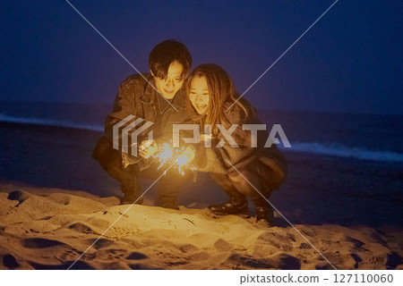 Young men and women playing hand-held fireworks on the beach at night 127110060