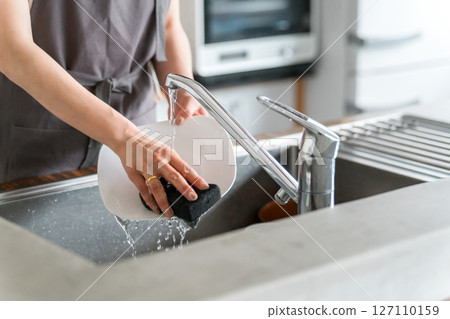Hands of a housewife washing dishes in the kitchen sink 127110159