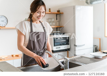A housewife in an apron washing dishes at the kitchen sink A housewife in an apron washing dishes at the kitchen sink 127110160