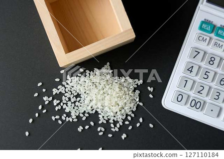 A little bit of rice spilled from a wooden box and a calculator 127110184