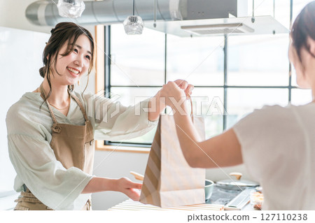 A female cafe attendant handing out takeaway items to customers at a cafe or restaurant A female cafe attendant handing out takeaway items to customers at a cafe or restaurant 127110238