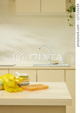 Yellow rubber gloves and cleaning supplies near the sink in a cozy beige kitchen, lifestyle in everyday household activities. Empty space for add text and display product 127110284