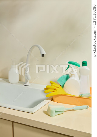 A sink filled with foam and dishes with bright yellow gloves and sponge on the side, representing active dishwashing in progress. Set of cleaning product with space for design 127110286