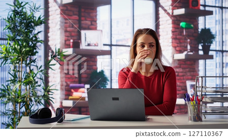 Casual focused woman sitting at her desk and reading research papers, multitasking with laptop at home office. Adult diving into professional or personal topics of improvement. Camera A. Casual focused woman sitting at her desk and reading research papers, multitasking with laptop at home office. Adult diving into professional or personal topics of improvement. Camera A. 127110367