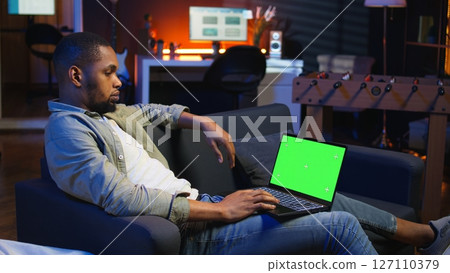 Confident young freelancer using isolated copy space in the living room, laying on his sofa in a modern living room decorated with neon lights and trendy furniture. Guy with gadgets. Camera A. Confident young freelancer using isolated copy space in the living room, laying on his sofa in a modern living room decorated with neon lights and trendy furniture. Guy with gadgets. Camera A. 127110379