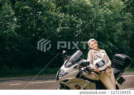 Stylish senior woman with gray hair and motorcycle posing on roadside, symbol of freedom and grace Stylish senior woman with gray hair and motorcycle posing on roadside, symbol of freedom and grace 127110435