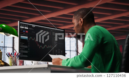 African american man using PC to purchase and sell stocks, monitoring forex graphs and diagrams. Male broker looking at stock exchange candle stick charts on computer. Camera A. African american man using PC to purchase and sell stocks, monitoring forex graphs and diagrams. Male broker looking at stock exchange candle stick charts on computer. Camera A. 127110436