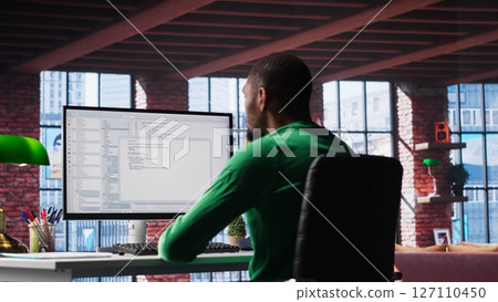 Black IT developer at PC coding and creating an app software, implementing algorithms to fix errors. Engineer in his loft working with code language, optimizing app performance. Camera B. Black IT developer at PC coding and creating an app software, implementing algorithms to fix errors. Engineer in his loft working with code language, optimizing app performance. Camera B. 127110450