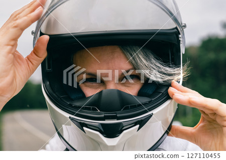 Close-up of mature woman in helmet with gray hair, symbol of confidence, freedom and timeless beauty Close-up of mature woman in helmet with gray hair, symbol of confidence, freedom and timeless beauty 127110455