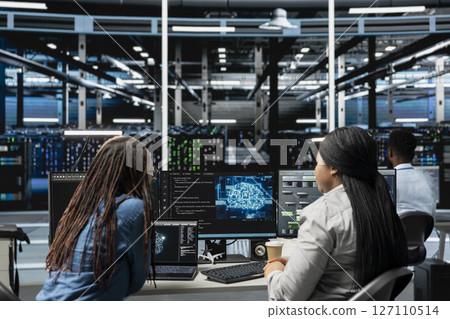 Data center engineering team working together, using AI visualization to oversee automated repetitive tasks. Server farm teamworking colleagues modifying systems based on data analytics graphs 127110514