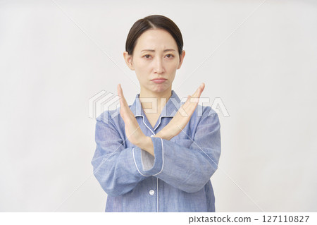 一位身穿睡衣的女士在白色背景上用手臂做出十字手勢 127110827