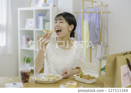 A young woman about to eat pizza in front of a table with food she ordered via delivery A young woman about to eat pizza in front of a table with food she ordered via delivery 127111169