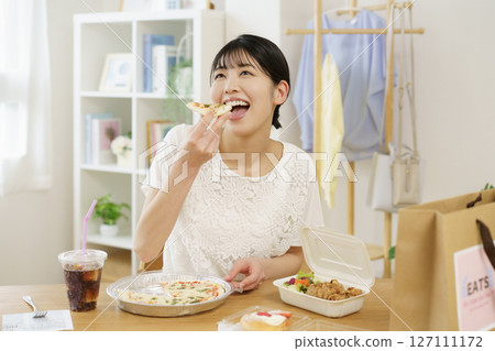 A young woman about to eat pizza in front of a table with food she ordered via delivery 127111172