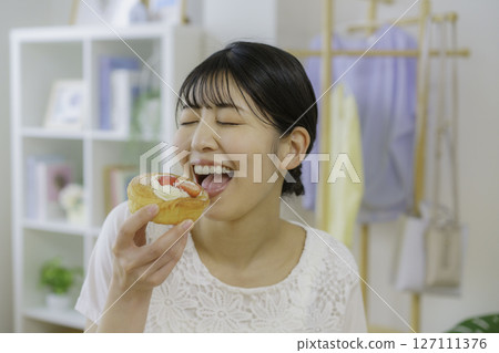 A young woman about to eat a sweet bun in the living room 127111376