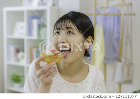 A young woman about to eat a sweet bun in the living room A young woman about to eat a sweet bun in the living room 127111377