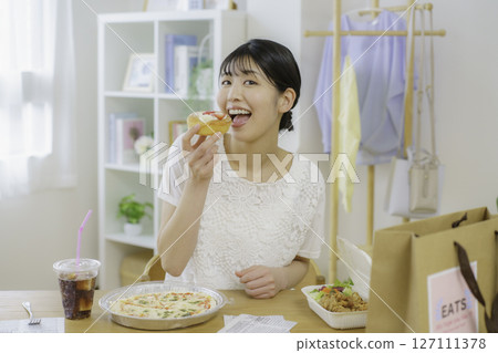 A young woman about to eat a sweet bun in front of a table with food she ordered via delivery A young woman about to eat a sweet bun in front of a table with food she ordered via delivery 127111378
