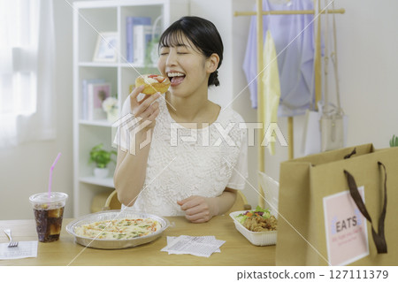 A young woman about to eat a sweet bun in front of a table with food she ordered via delivery 127111379