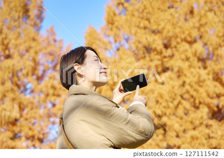 Middle-aged woman taking photos of autumn leaves Middle-aged woman taking photos of autumn leaves 127111542