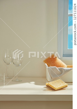 An orange sponge sits next to a handkerchief and a glass of wine on a beige table in natural light, capturing a moment of pause while cleaning. Space for cleaning products An orange sponge sits next to a handkerchief and a glass of wine on a beige table in natural light, capturing a moment of pause while cleaning. Space for cleaning products 127111824