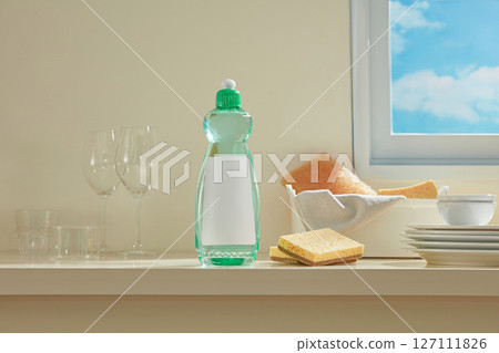 Bottle of dish soap and stacked glasses near a window, accompanied by sponges and light reflections that suggest a refreshed kitchen vibe. 127111826